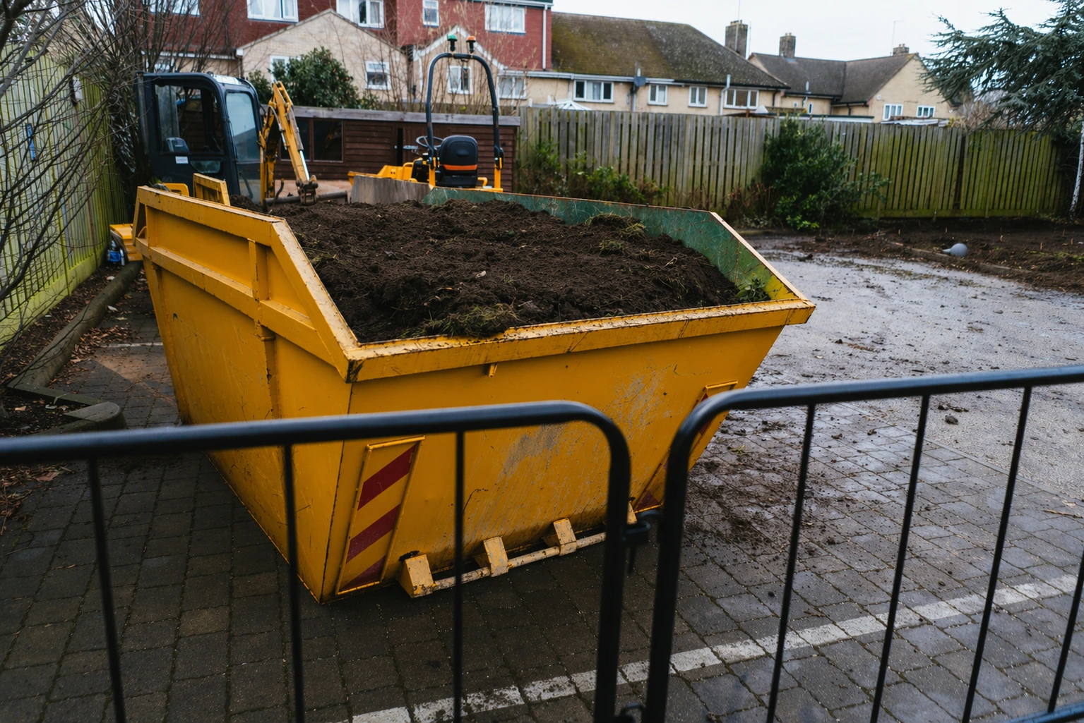 Large yellow skip bin filled with soil at a residential construction site, showing typical usage for understanding how much it costs to buy a skip for waste removal projects.